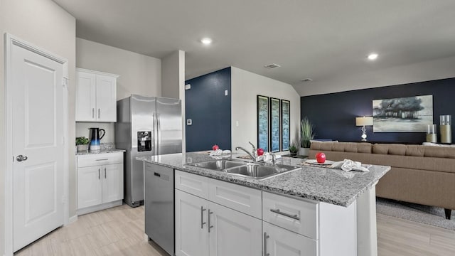 kitchen featuring appliances with stainless steel finishes, open floor plan, white cabinets, a sink, and an island with sink