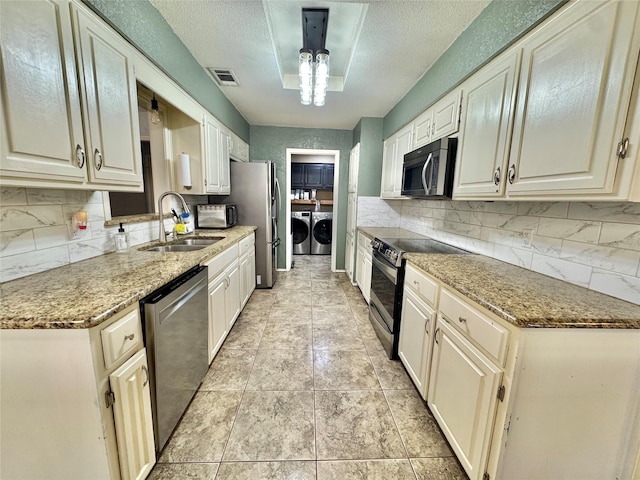 kitchen featuring washing machine and dryer, appliances with stainless steel finishes, decorative backsplash, and a sink