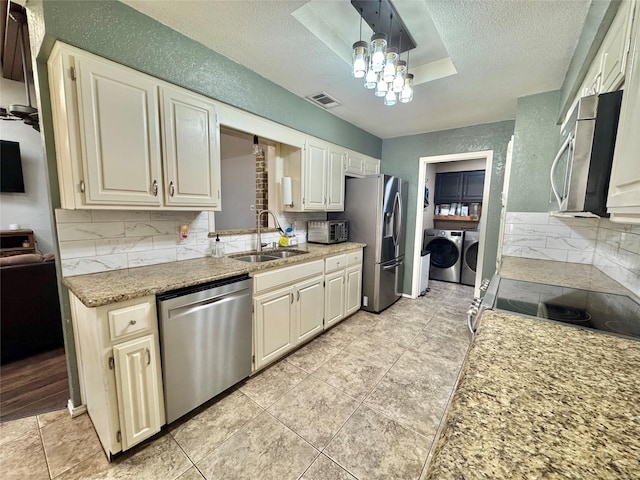 kitchen featuring visible vents, stainless steel appliances, a textured ceiling, washer and dryer, and a sink