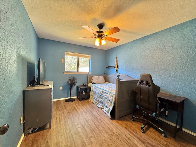 bedroom with baseboards, wood finished floors, and a textured wall