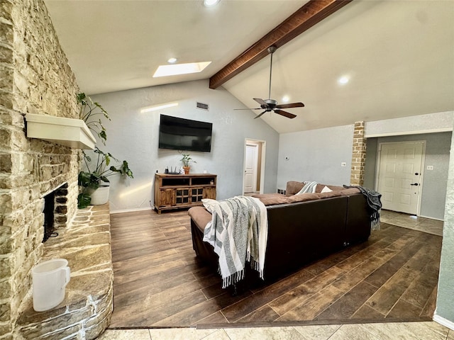 living room with ceiling fan, vaulted ceiling with skylight, a stone fireplace, recessed lighting, and wood finished floors