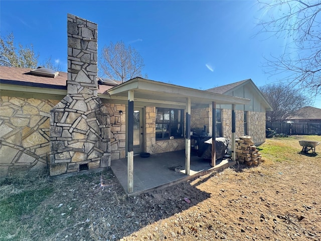 rear view of property with a patio, a shingled roof, fence, stone siding, and a chimney