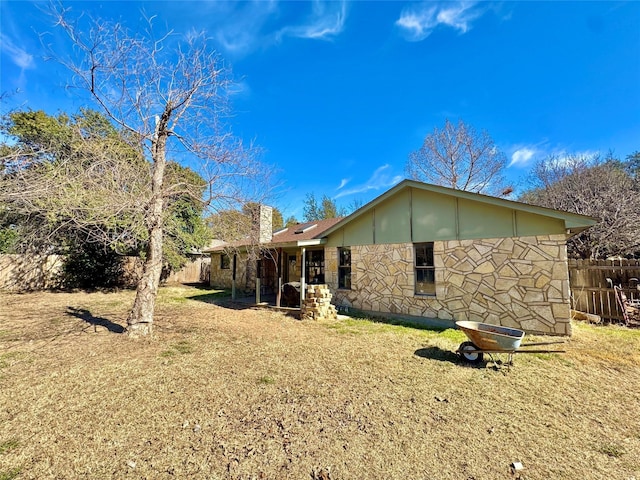 rear view of property featuring stone siding, a yard, a chimney, and fence