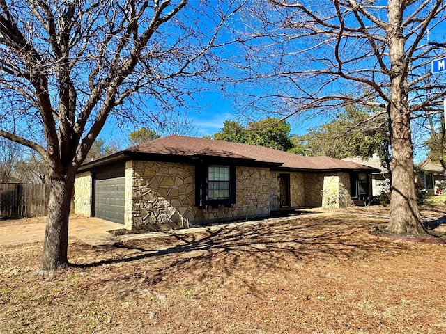 view of side of home with an attached garage, stone siding, fence, and concrete driveway