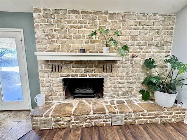 interior details featuring a brick fireplace, wood finished floors, visible vents, and baseboards