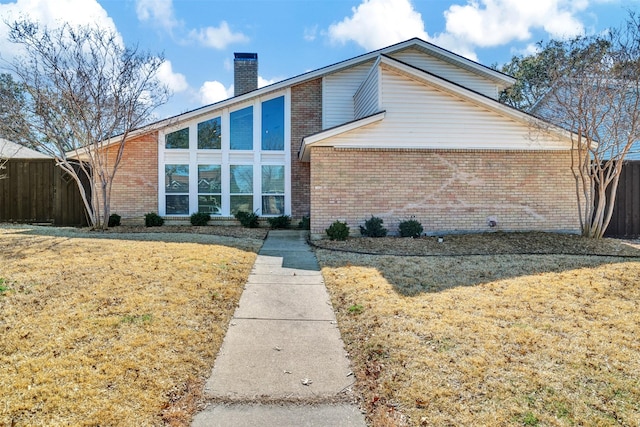 view of side of property with a chimney, fence, a lawn, and brick siding