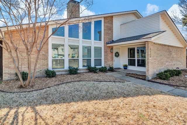 view of front of home with a front yard, brick siding, and a chimney