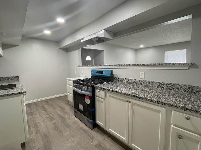 kitchen with under cabinet range hood, wood finished floors, baseboards, stainless steel gas range, and dark stone countertops