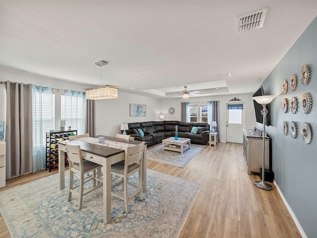 dining space with light wood finished floors, baseboards, visible vents, a raised ceiling, and a ceiling fan