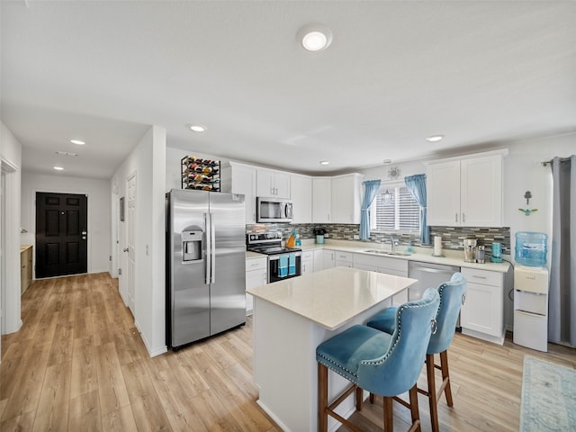 kitchen featuring a center island, stainless steel appliances, light countertops, white cabinetry, and a sink