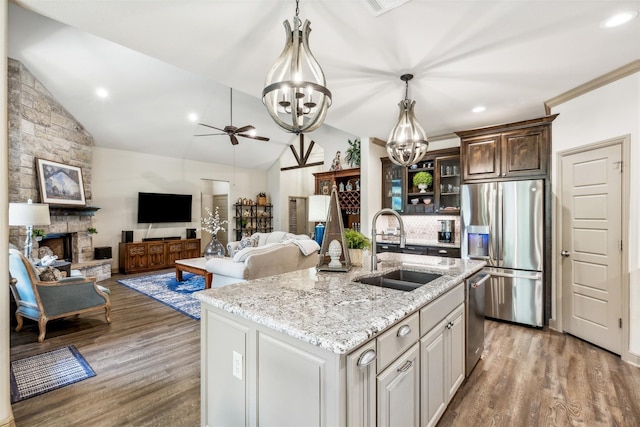 kitchen featuring appliances with stainless steel finishes, glass insert cabinets, dark brown cabinetry, a sink, and an island with sink