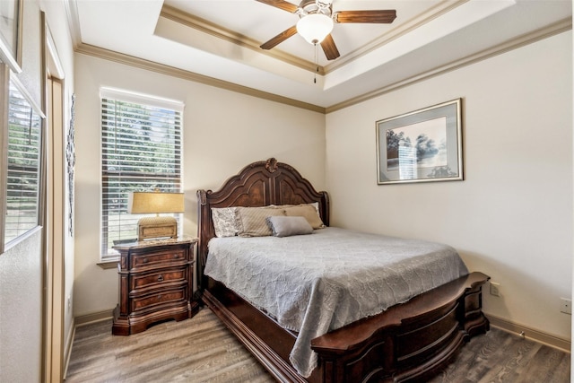 bedroom with baseboards, a tray ceiling, wood finished floors, and crown molding