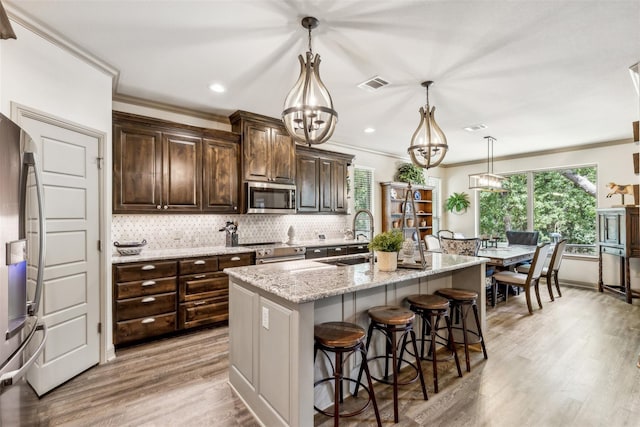 kitchen with stainless steel appliances, a sink, visible vents, a center island with sink, and pendant lighting