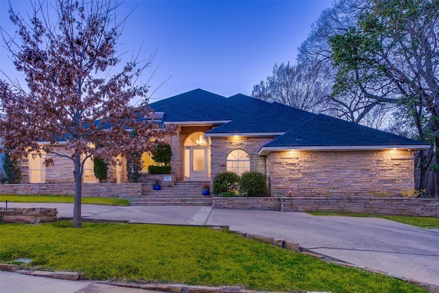 view of front of home featuring stone siding, a shingled roof, and a lawn