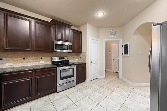 2601 Sabine Cir, Royse City, TX 75189 - kitchen featuring stainless steel appliances, decorative backsplash, dark stone countertops, dark brown cabinetry, and baseboards