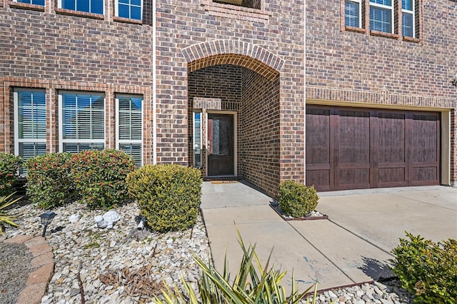 doorway to property featuring driveway, a garage, and brick siding