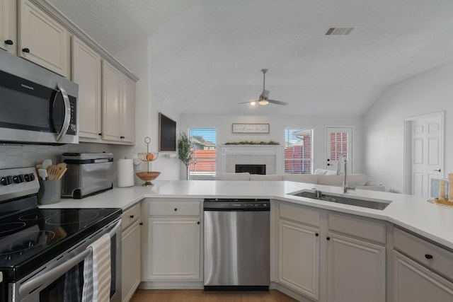 kitchen featuring stainless steel appliances, a peninsula, a sink, open floor plan, and light countertops