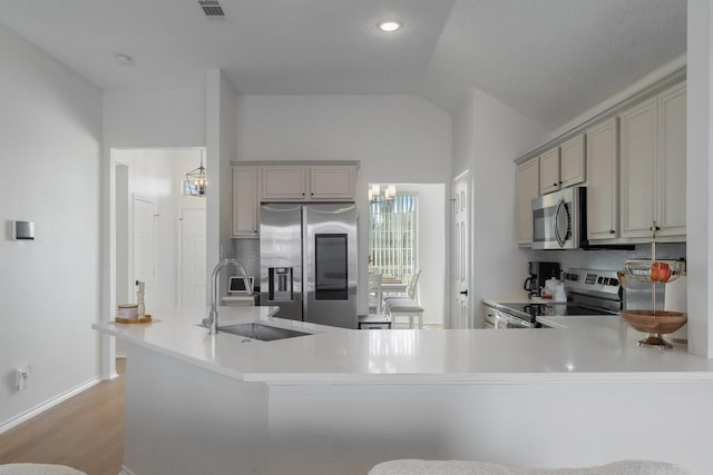 kitchen with light countertops, appliances with stainless steel finishes, a peninsula, and a sink