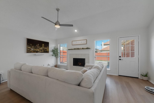 living area with light wood-type flooring, a fireplace, a wealth of natural light, and a ceiling fan