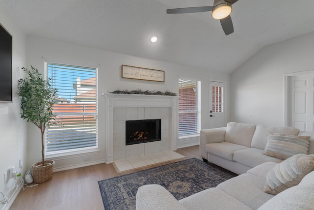 living room with lofted ceiling, a tile fireplace, wood finished floors, a ceiling fan, and baseboards