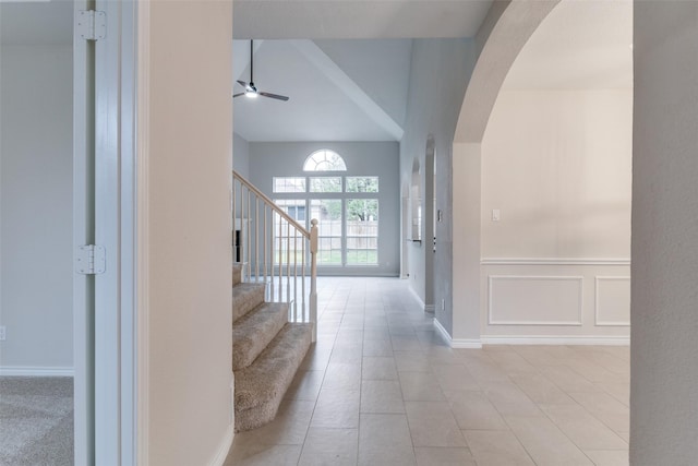 entrance foyer featuring arched walkways, ceiling fan, a decorative wall, a wainscoted wall, and stairway