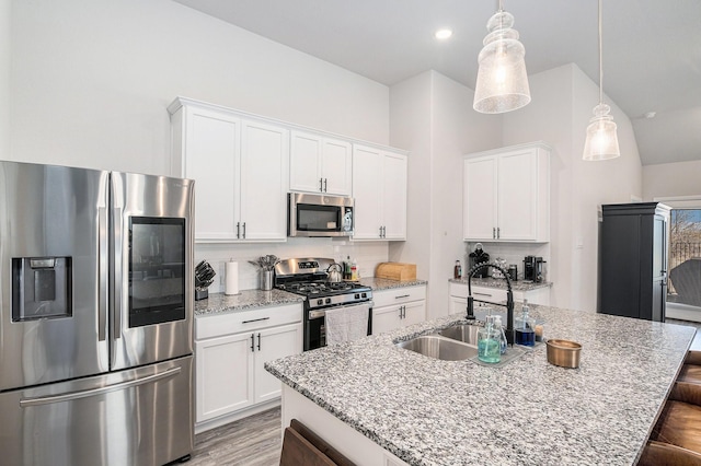 kitchen featuring white cabinets, appliances with stainless steel finishes, a breakfast bar, decorative light fixtures, and a sink