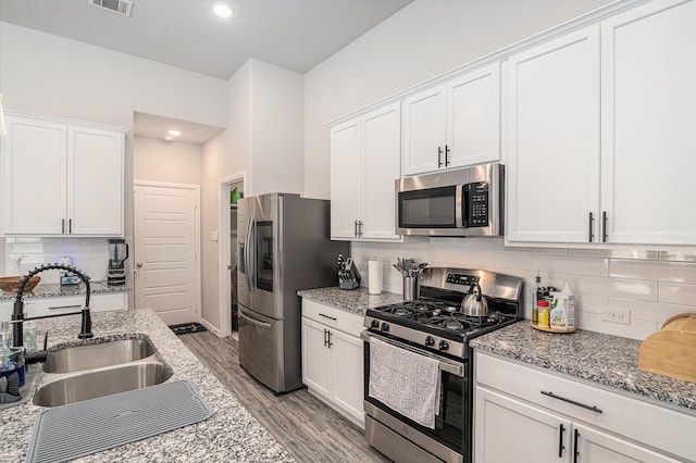 kitchen with stainless steel appliances, light stone counters, a sink, and white cabinetry