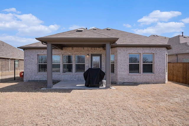 back of house with a patio area, a fenced backyard, roof with shingles, and brick siding