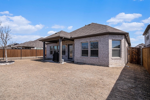 back of house with brick siding, a patio area, a fenced backyard, and a shingled roof