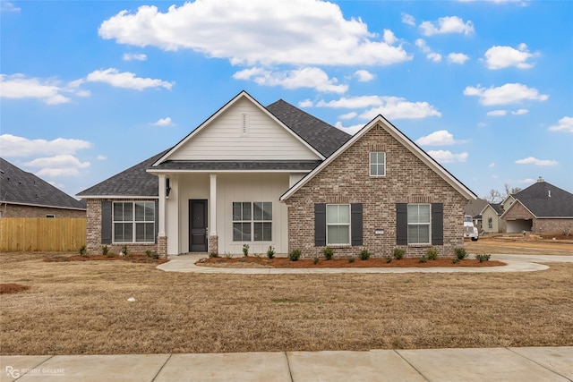 view of front of property featuring a shingled roof, a front yard, brick siding, and fence