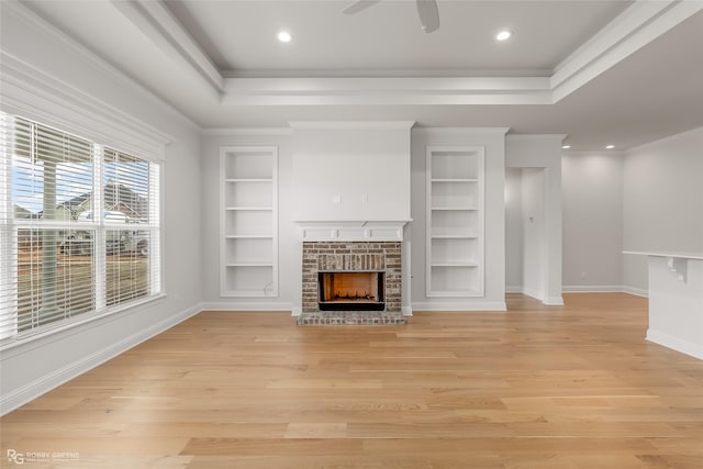 unfurnished living room featuring a tray ceiling, light wood-type flooring, built in shelves, and baseboards