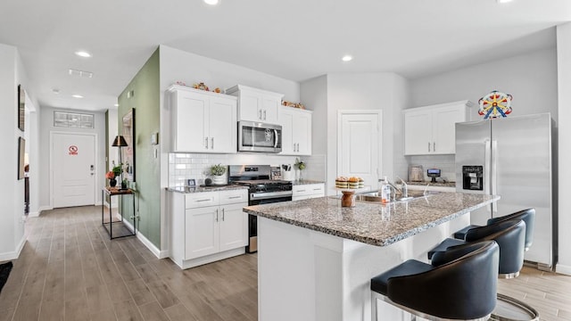 kitchen with appliances with stainless steel finishes, white cabinets, a center island with sink, and a sink