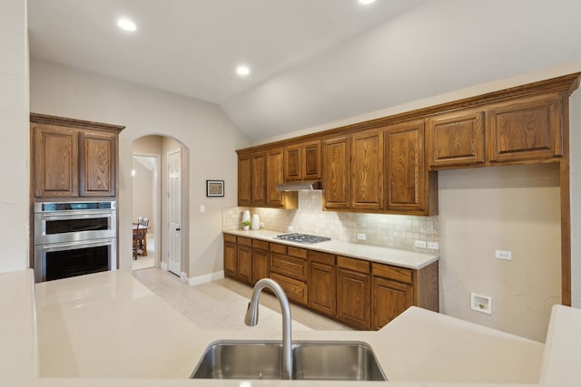 kitchen with arched walkways, tasteful backsplash, appliances with stainless steel finishes, a sink, and under cabinet range hood