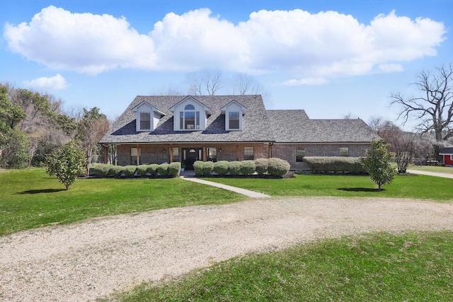 new england style home with brick siding, driveway, a front yard, and roof with shingles