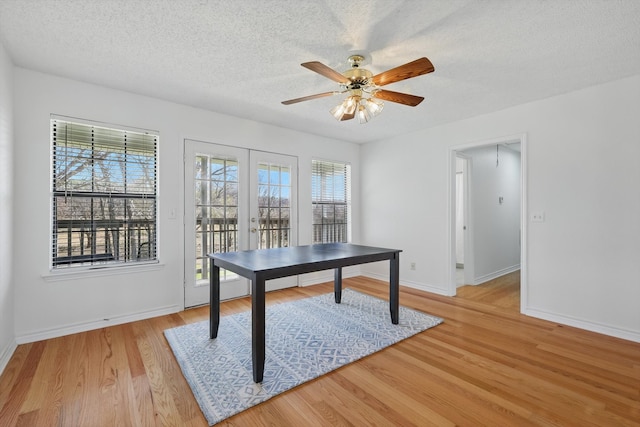 unfurnished office with light wood-type flooring, a ceiling fan, a textured ceiling, french doors, and baseboards