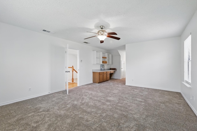 unfurnished living room featuring light carpet, visible vents, a textured ceiling, and built in desk