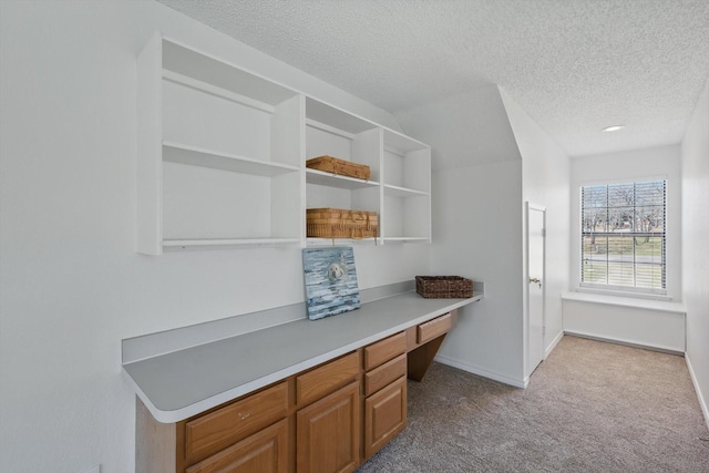 office space with built in desk, light colored carpet, a textured ceiling, and baseboards