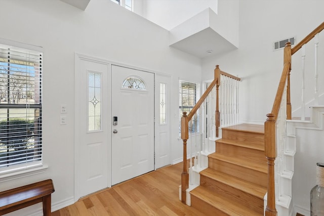 foyer featuring light wood finished floors, visible vents, stairway, and a high ceiling