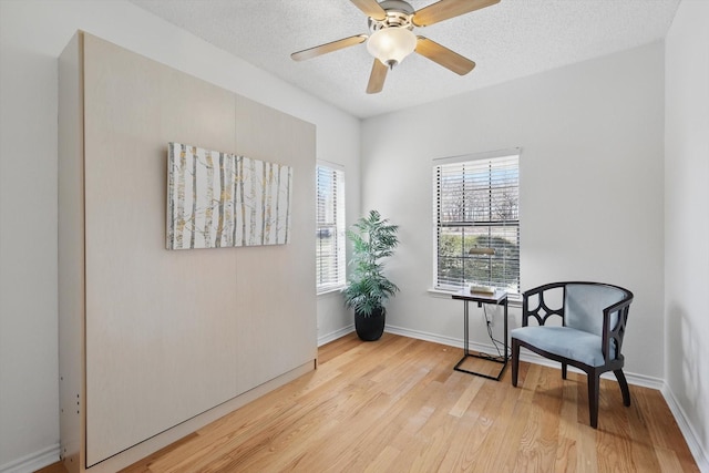 sitting room with baseboards, ceiling fan, a textured ceiling, and light wood-style floors