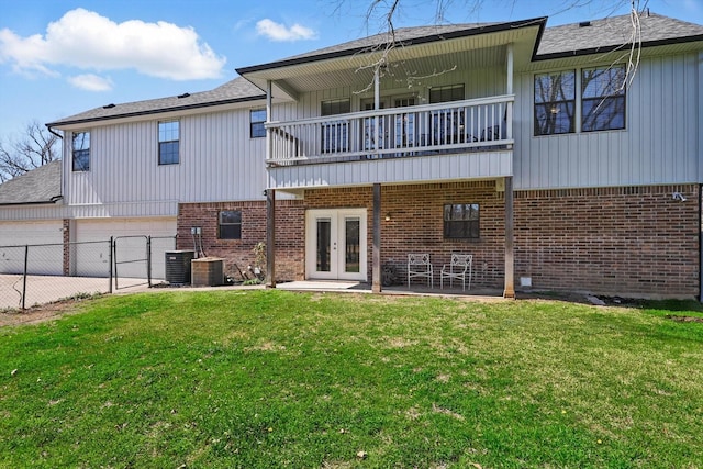 rear view of property with a balcony, fence, a yard, french doors, and brick siding