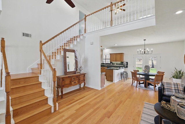 interior space featuring visible vents, baseboards, ceiling fan with notable chandelier, a high ceiling, and wood finished floors