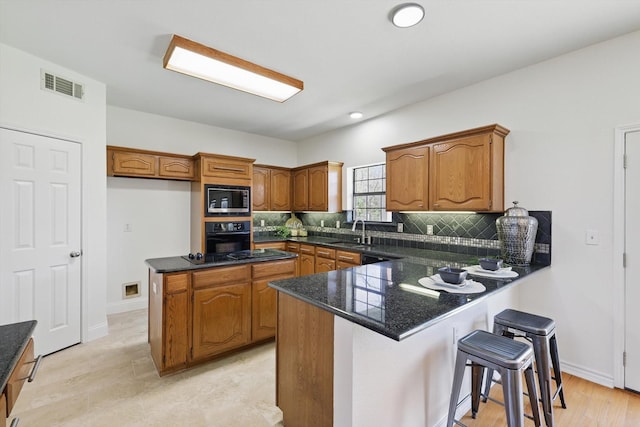 kitchen featuring visible vents, backsplash, brown cabinets, a peninsula, and black appliances