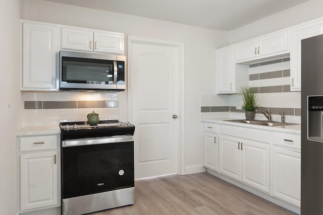 kitchen featuring decorative backsplash, white cabinets, appliances with stainless steel finishes, light wood-style floors, and a sink