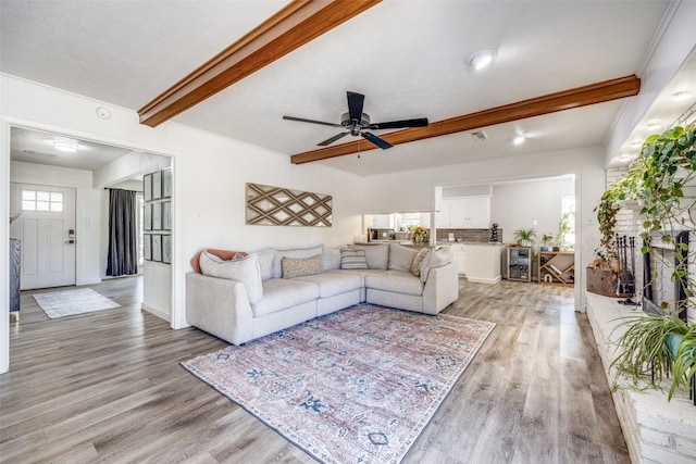 living room with beverage cooler, beamed ceiling, light wood-type flooring, and a ceiling fan