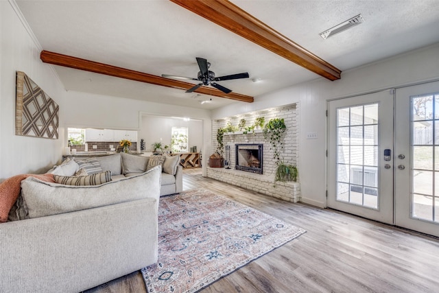 living area featuring visible vents, wood finished floors, french doors, a brick fireplace, and beam ceiling