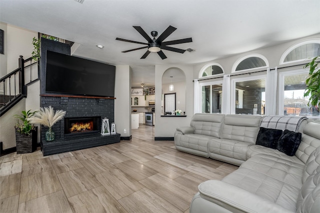 living room featuring visible vents, baseboards, stairs, a ceiling fan, and a brick fireplace