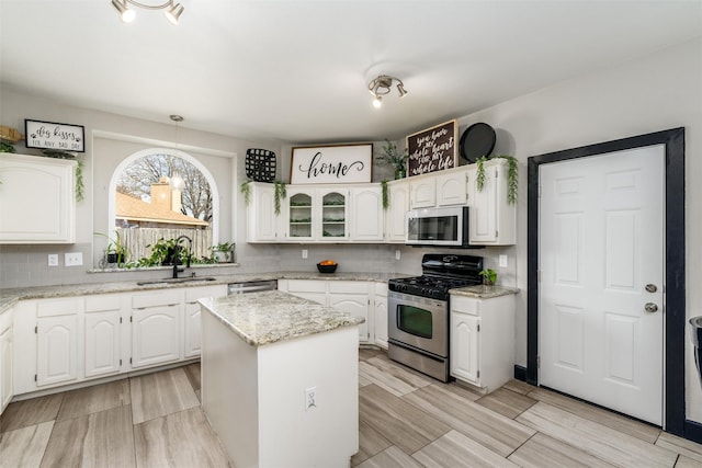 kitchen featuring stainless steel appliances, a sink, white cabinets, a center island, and decorative light fixtures