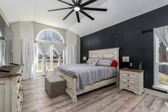 bedroom with light wood finished floors, an accent wall, a ceiling fan, vaulted ceiling, and baseboards