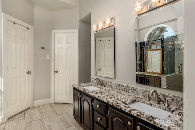 full bathroom with double vanity, a shower stall, baseboards, and a sink