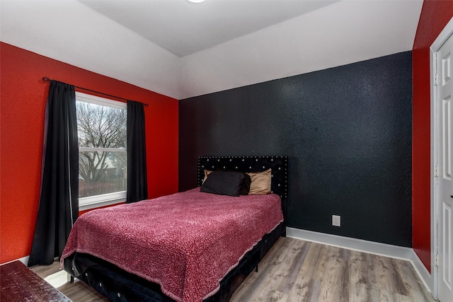 bedroom featuring lofted ceiling, baseboards, and wood finished floors